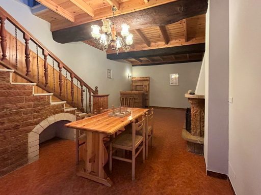 Spaziosa sala con camino, tavolo da pranzo, soffitto in legno e scala che collega il piano inferiore della casa