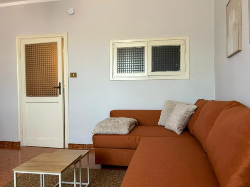 Divano ad angolo vicino alla porta del soggiorno, con finestra interna e tavolino.